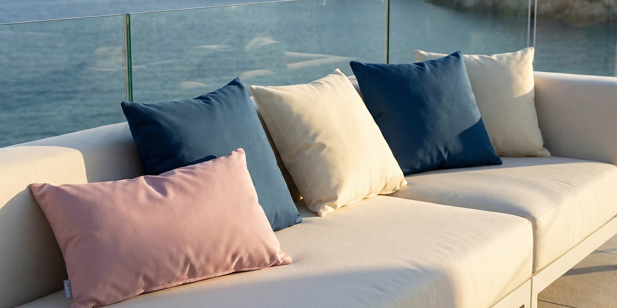 Outdoor sofa cushions on a terrace with pastel and navy cushions overlooking the water