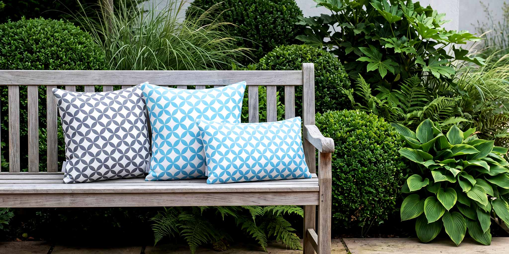 Blue and grey Bahia Marrakech outdoor cushions on a weathered teak bench in a British courtyard garden