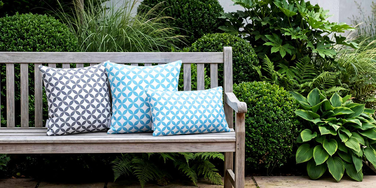 Blue and grey Bahia Marrakech outdoor cushions on a weathered teak bench in a British courtyard garden