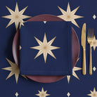 Navy and gold Stars Christmas napkin folded in four on a plum plate, laid on the matching Stars tablecloth with brass cutlery