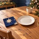 Navy and gold Stars cotton napkin in a compact square fold beside a dinner plate and coffee cup on a wooden table in daylight.