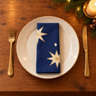 Navy and gold Stars cotton napkin neatly folded on a dinner plate with cutlery and candlelight on a wooden Christmas table.