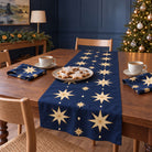 Stars Christmas table runner in Navy and gold, styled on a wooden table with a softly draped end in a daylight Christmas room.