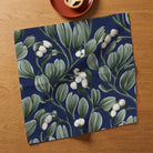 Navy Mistletoe Christmas napkin opened on an oak table, with a mince pie on a terracotta plate above.