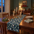 Mistletoe Christmas table runner in Navy, styled on a wooden table with a softly draped end in a candlelit Christmas room.