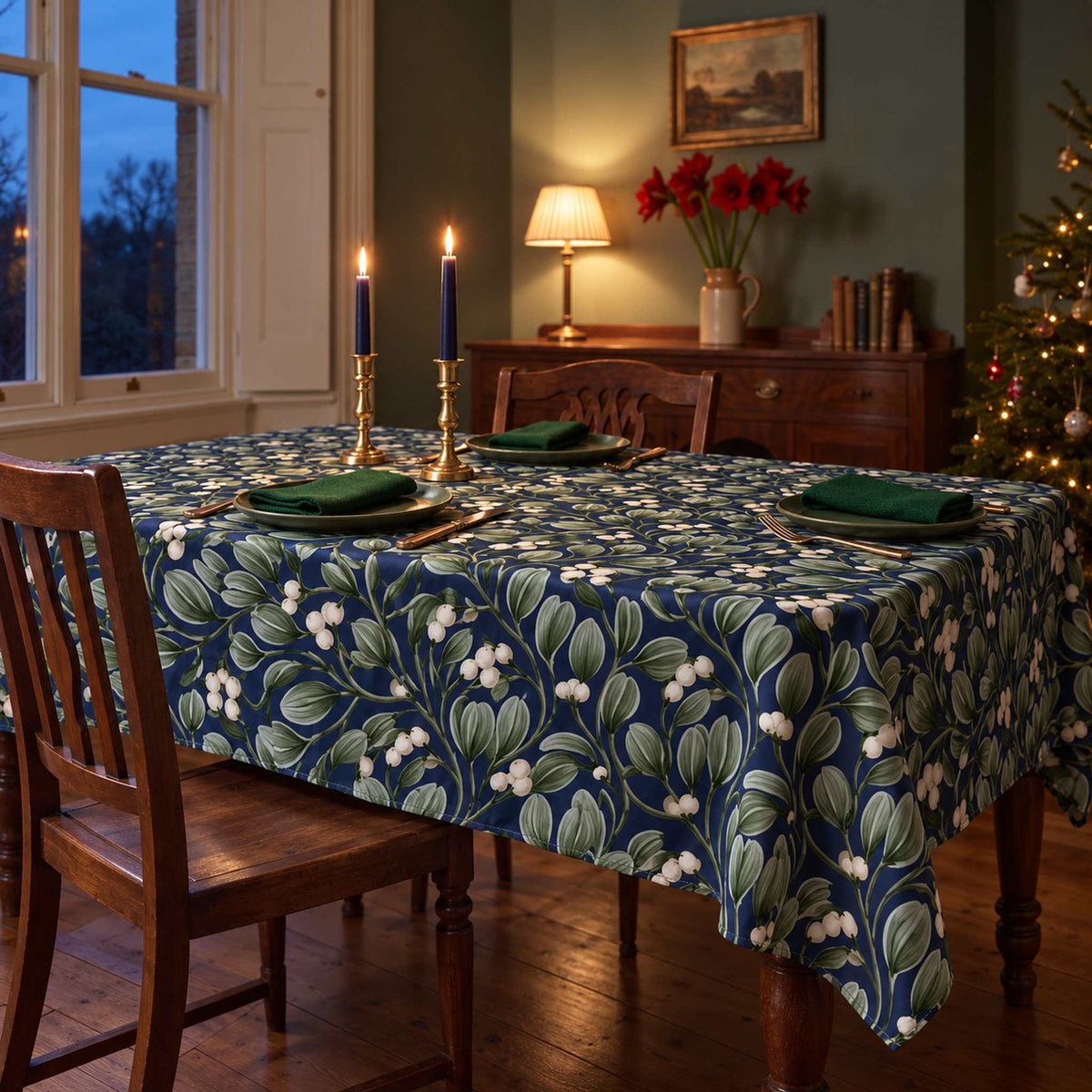 Navy Mistletoe Christmas tablecloth draped over a dining table with green plates and navy candles in a green Victorian dining room.