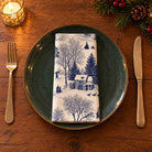 Navy on ivory Village Toile cotton napkin neatly folded on a dinner plate with cutlery and candlelight on a wooden Christmas table.