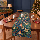 Robins and Christmas Roses Christmas table runner in Navy, styled on a wooden table with a softly draped end in a daylight Christmas room.