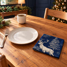 Navy Stag Woodland cotton napkin in a compact square fold beside a dinner plate and coffee cup on a wooden table in daylight.