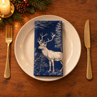 Navy Stag Woodland cotton napkin neatly folded on a dinner plate with cutlery and candlelight on a wooden Christmas table.