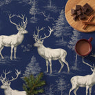 Navy Stag Woodland Christmas tablecloth seen from above, with a burgundy mug of hot chocolate, broken dark chocolate and cinnamon sticks on an oak board and a sprig of fir