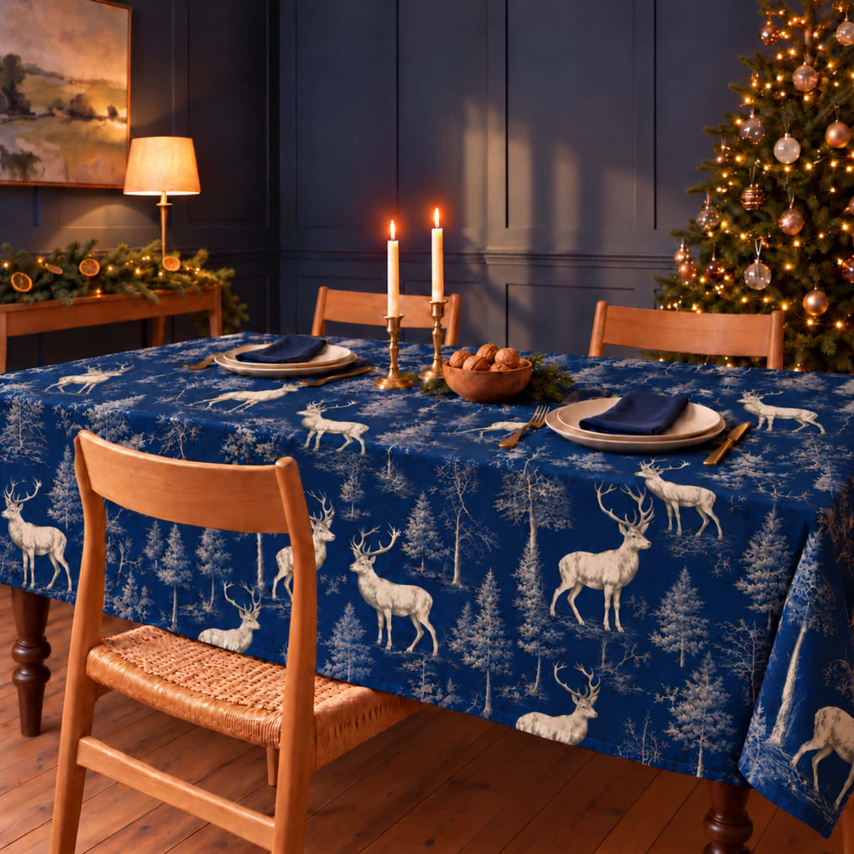 Navy Stag Woodland Christmas tablecloth draped over a dining table with navy napkins, ivory plates, walnuts and candles in a navy-panelled room.