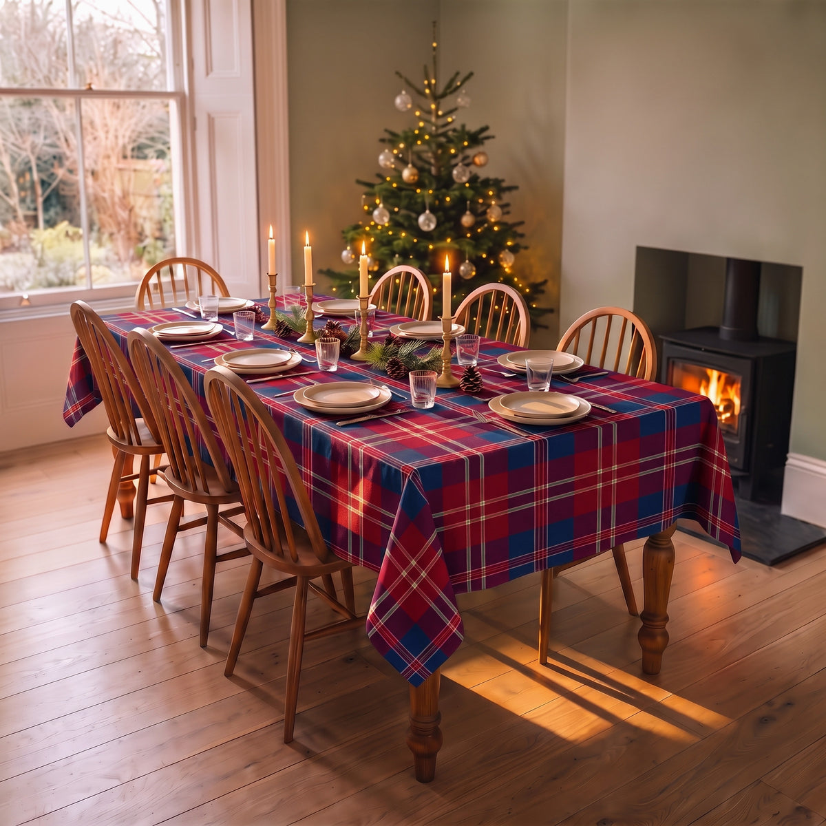 Navy tartan Christmas tablecloth on a dining table laid for Christmas, beside a decorated tree and a lit wood burner
