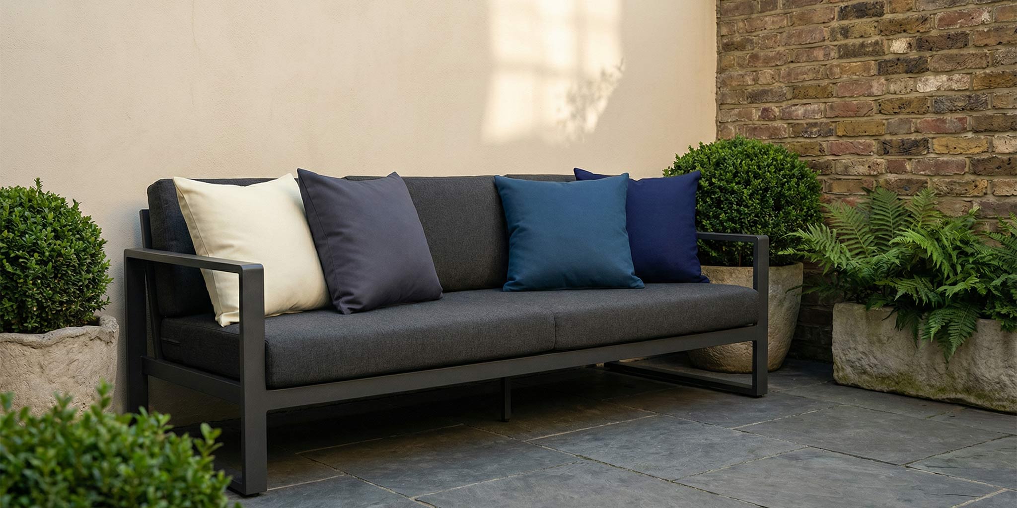 Outdoor garden cushions in Midnight, Estate Blue, Graphite and Ivory Cream by Izabela Peters styled on a charcoal sofa in a terrace garden
