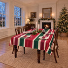 Red, green and burgundy Signature Stripe Christmas tablecloth on a dining table laid for four, with candles, red wine and a log fire in a Georgian dining room