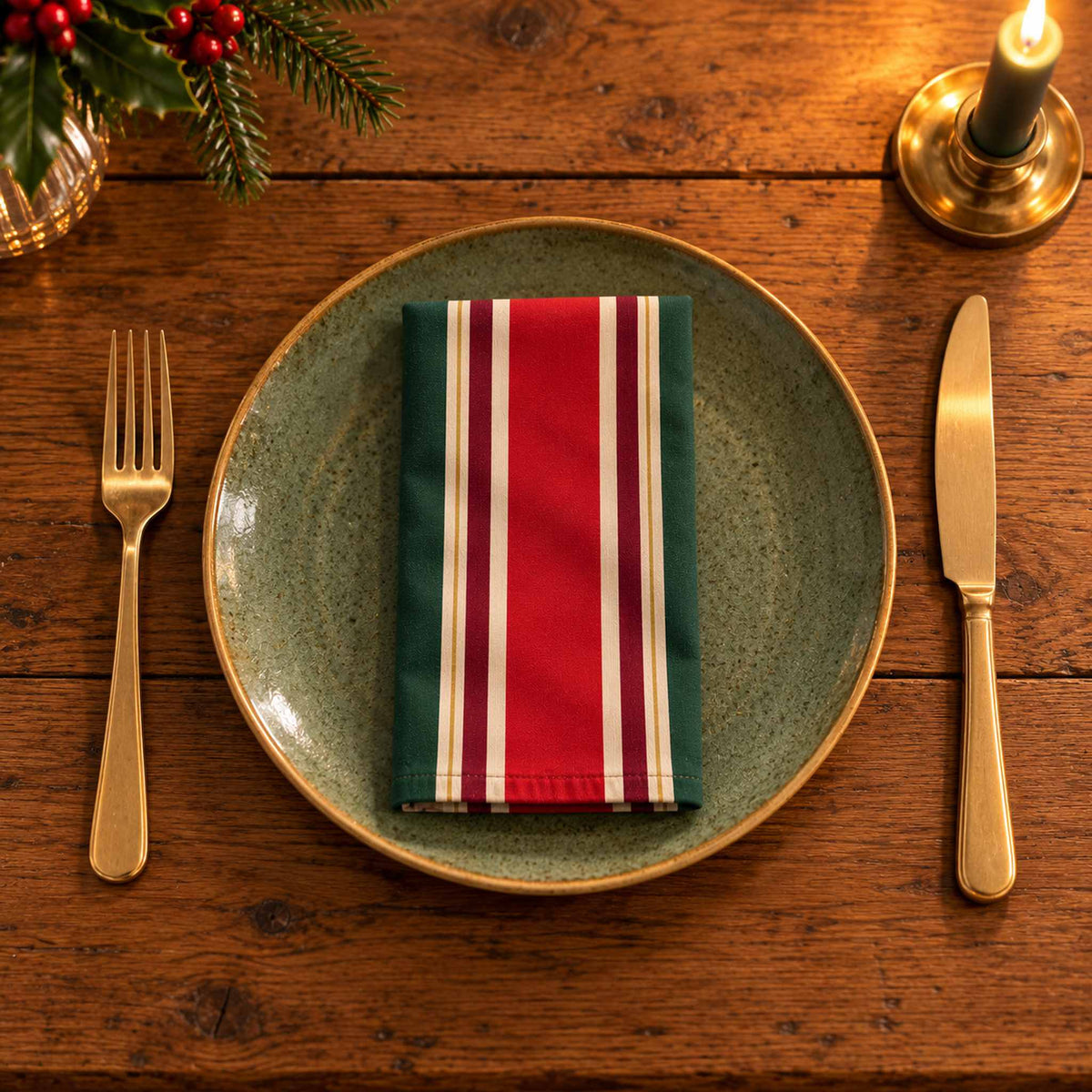 Red, green and burgundy Signature Stripe cotton napkin neatly folded on a dinner plate with cutlery and candlelight on a wooden Christmas table.