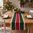Signature Stripe Christmas table runner in Red, green and burgundy, styled on a wooden table with a softly draped end in a daylight Christmas room.