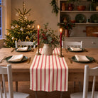 Ticking Stripe Christmas table runner in Red on ivory, styled on a wooden table with a softly draped end in a candlelit Christmas room.