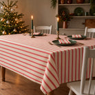 Red on ivory Ticking Stripe Christmas tablecloth with continuous lengthwise stripes, styled with green plates, striped napkins and candlelight in a cream farmhouse room.