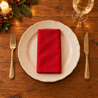 Red Plain cotton napkin neatly folded on a dinner plate with cutlery and candlelight on a wooden Christmas table.