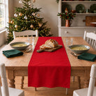 Plain Colours Christmas table runner in Red, styled on a wooden table with a softly draped end in a daylight Christmas room.