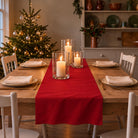 Plain Colours Christmas table runner in Red, styled on a wooden table with a softly draped end in a candlelit Christmas room.